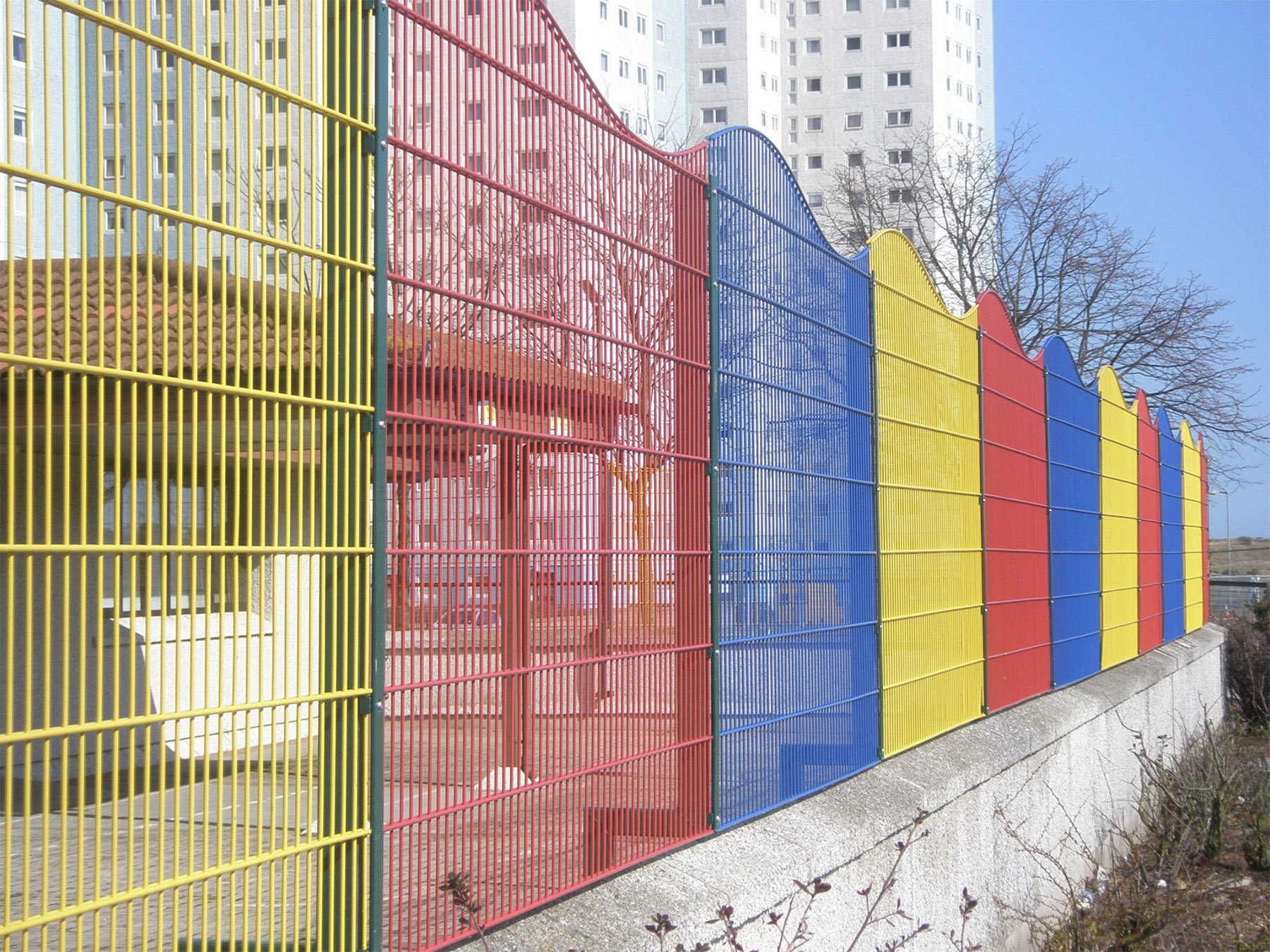 A decorative wave top fence installed above a wall using cranked posts at a school for children with complex needs. Multi-coloured panels were used to enhance the sensory appeal of the fence.