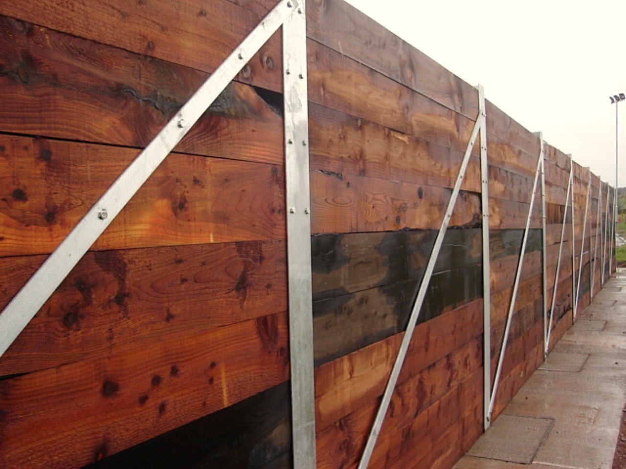 Retaining wall to a storage bay at a recycling centre formed using timber sleepers set between galvanised UC posts.