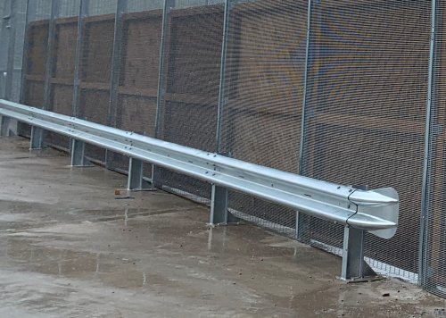Corrugated beam barrier on base plated posts. The barrier is fitted with a fishtail end.